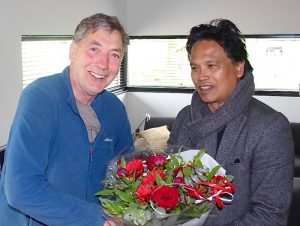 foto: De heer Van Emmerik ontvangt van Henri Jansen het jubileumspeldje en een bos bloemen